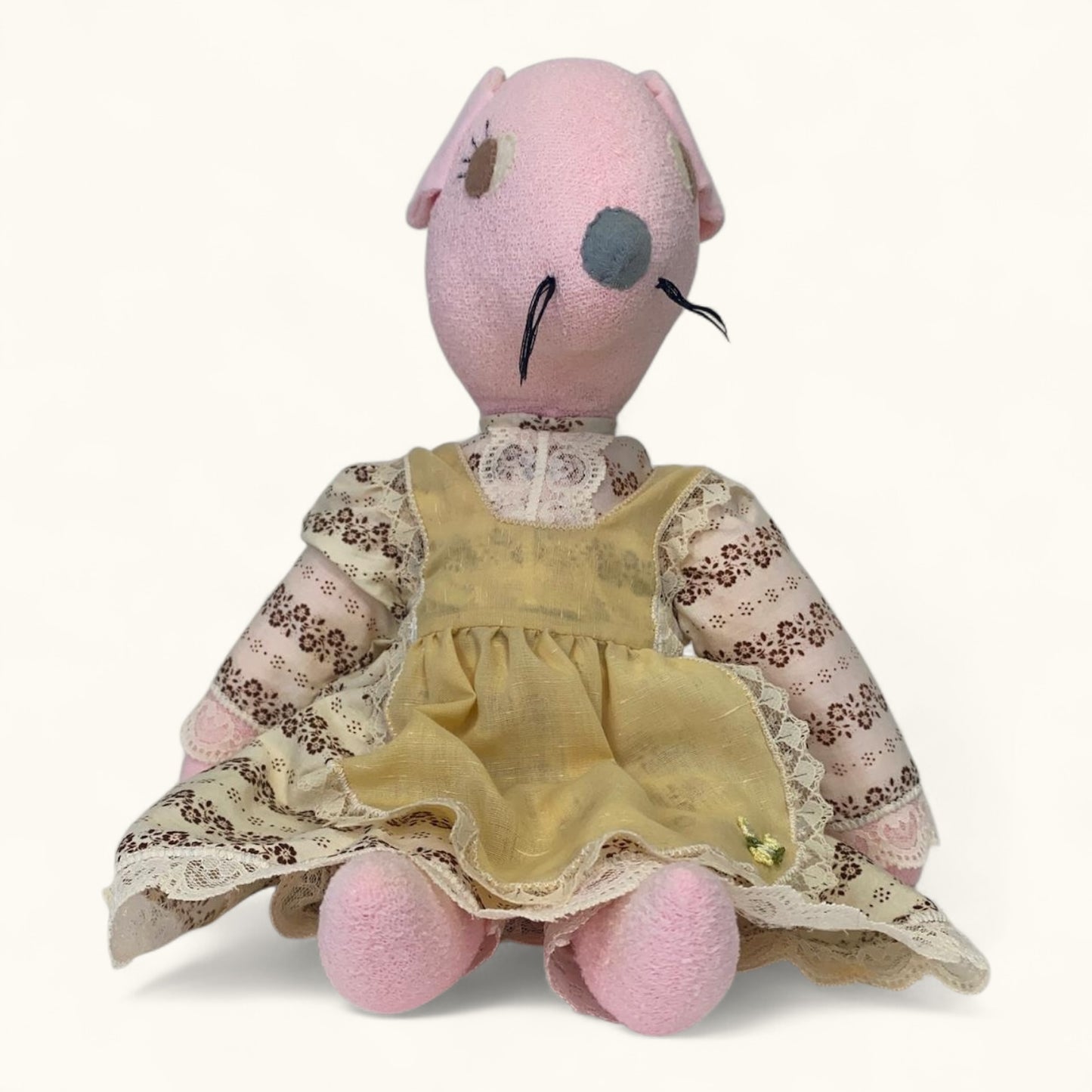 Stuffed animal toy with a pink head and yellow dress on a white background