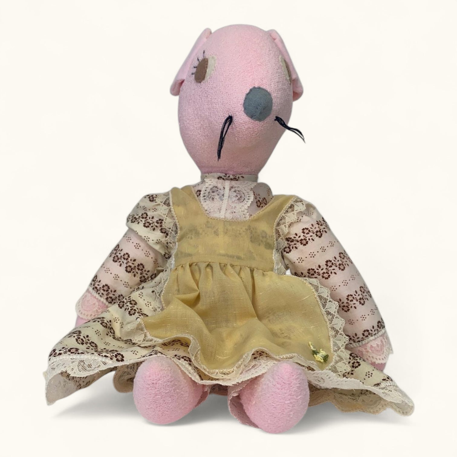 Stuffed animal toy with a pink head and yellow dress on a white background