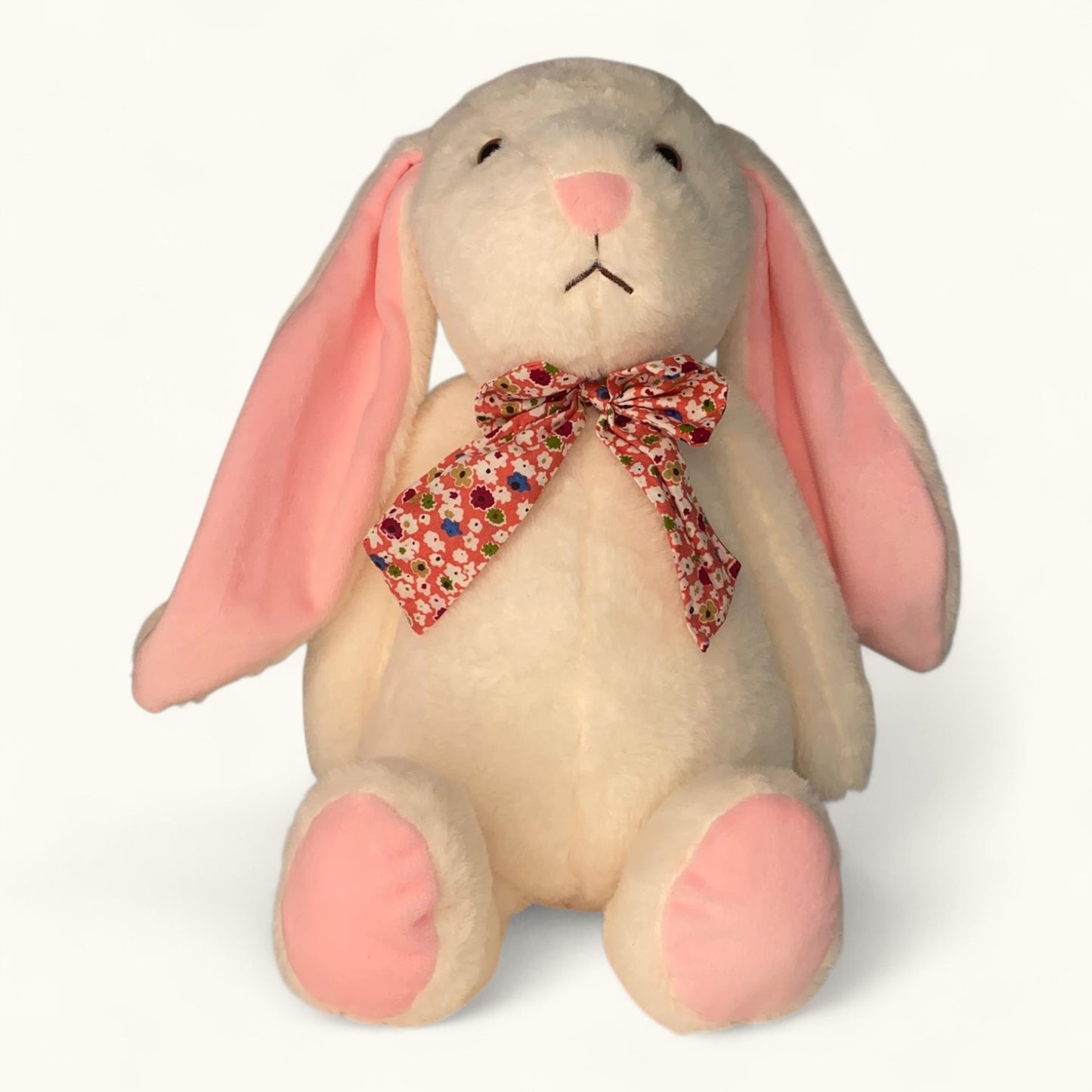 Stuffed bunny toy with pink ears and a floral bow tie on a white background