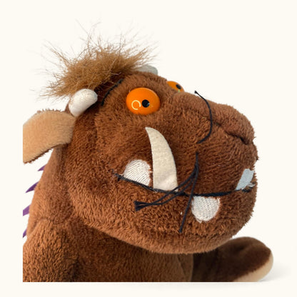 Plush toy resembling a character with a brown face, orange eyes, and white tusks on a white background.