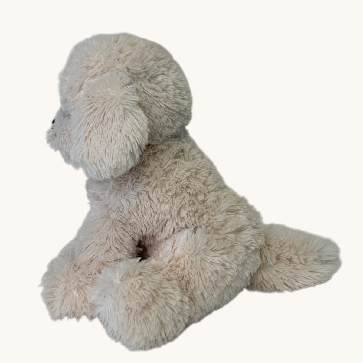 A plush dog toy with fluffy cream-colored faux fur, shown from the side against a plain off-white background.