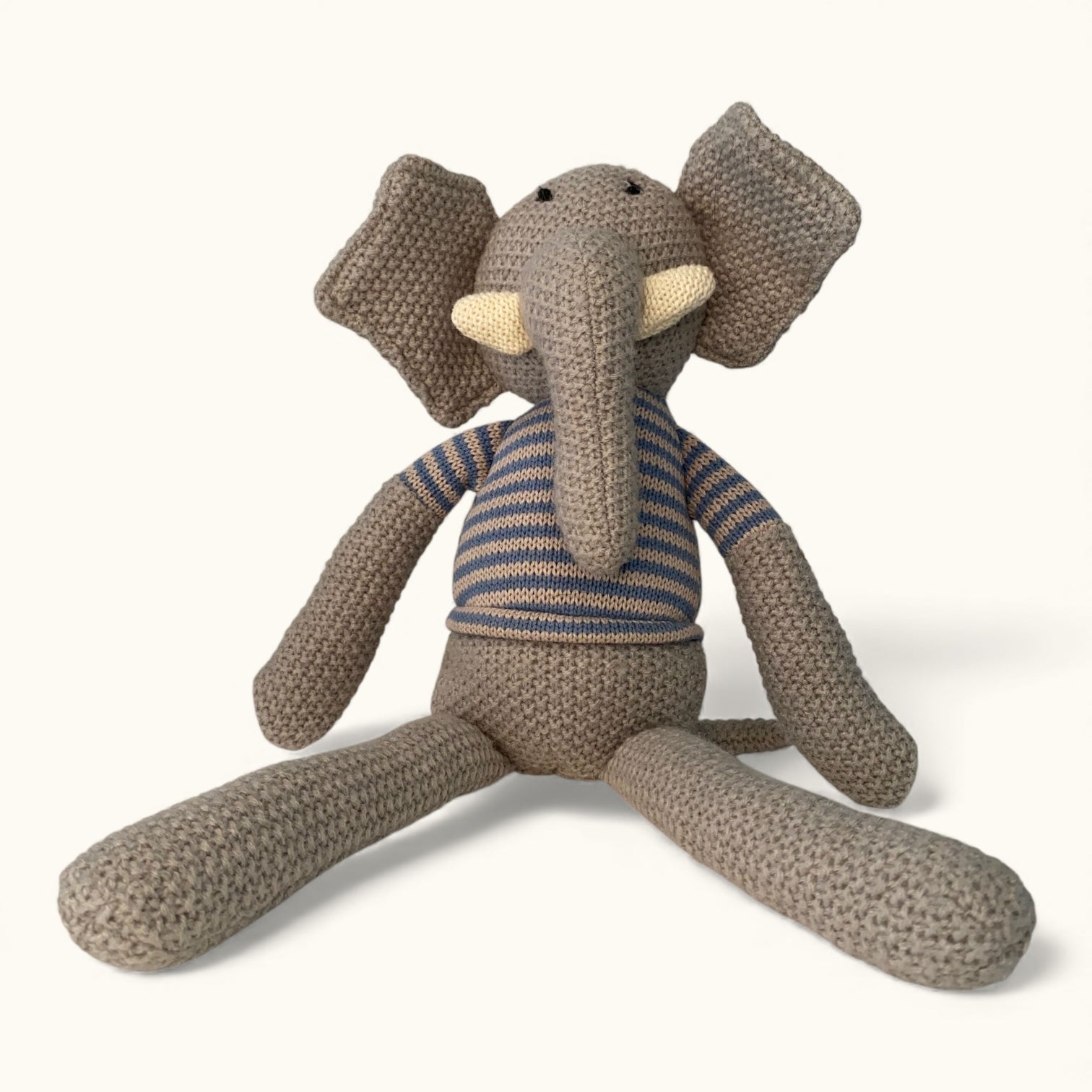 Knitted toy elephant wearing a striped sweater on a white background
