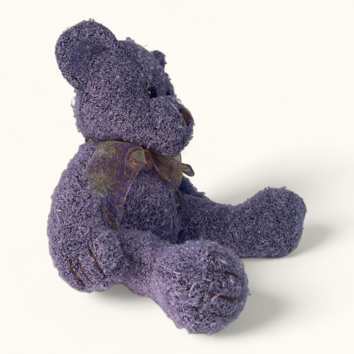 Purple teddy bear with a brown bow on a white background