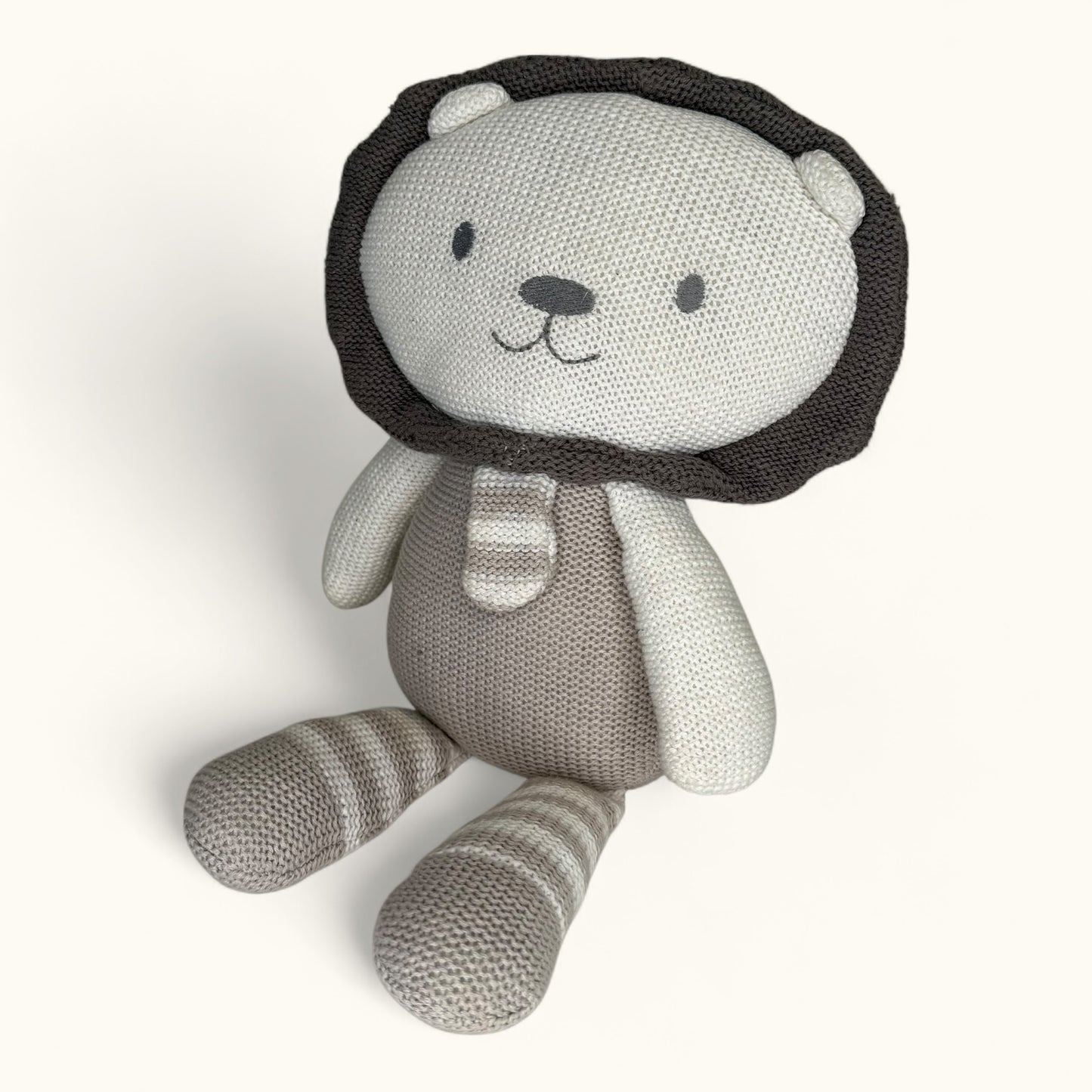 Knitted toy lion with a lion head and striped body on a white background