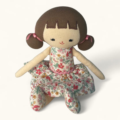 Stuffed doll with brown hair, floral dress, and pink buns on a white background