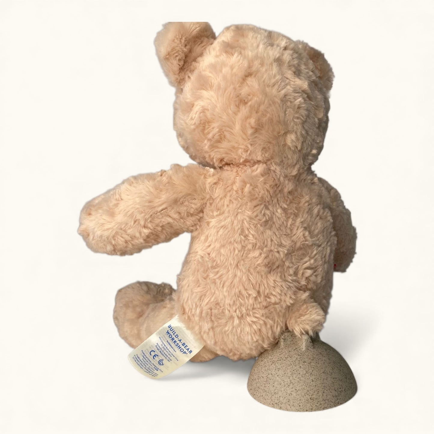 Beige teddy bear with a visible tag on a white background