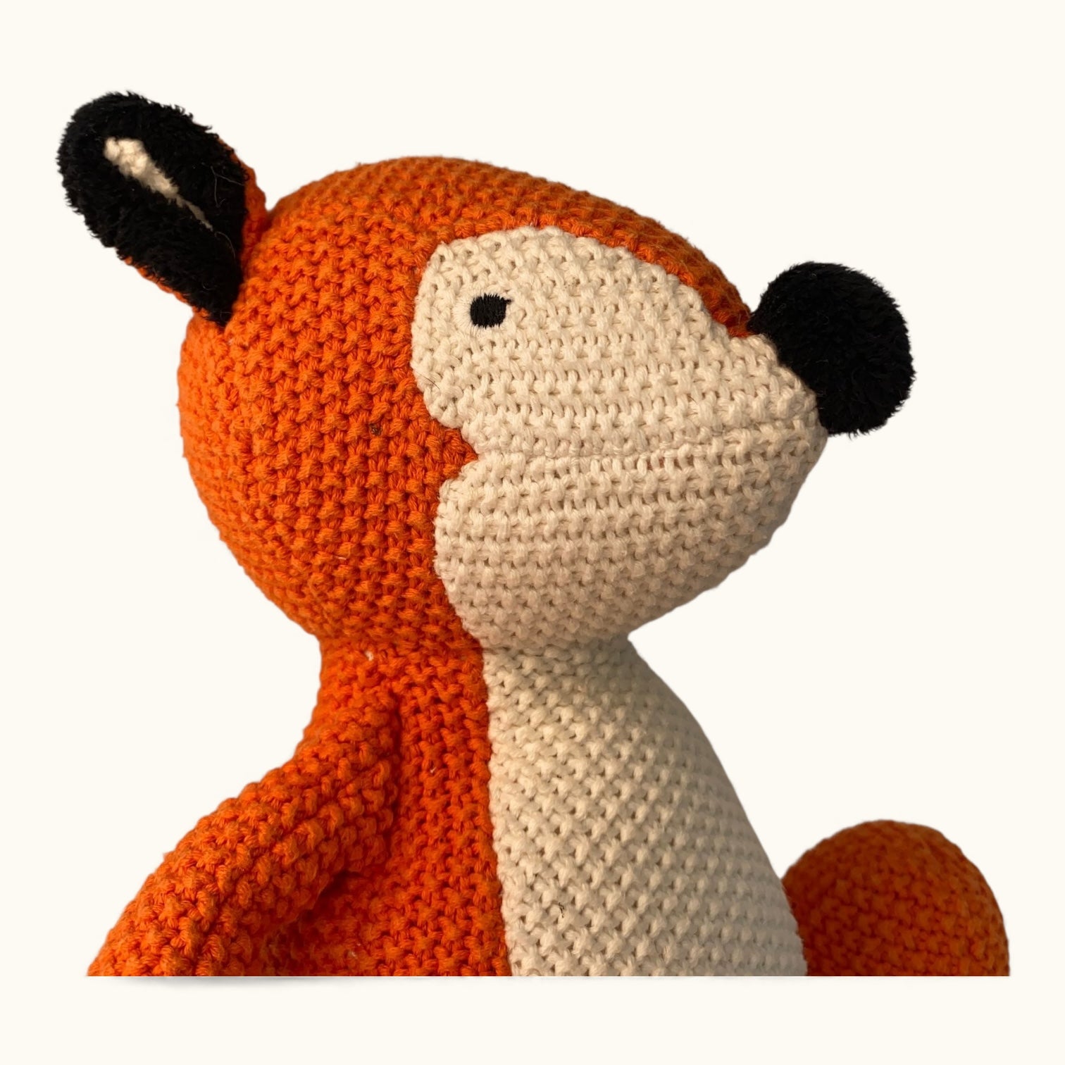 Crocheted fox toy with orange fur, black ears, and white muzzle on a white background