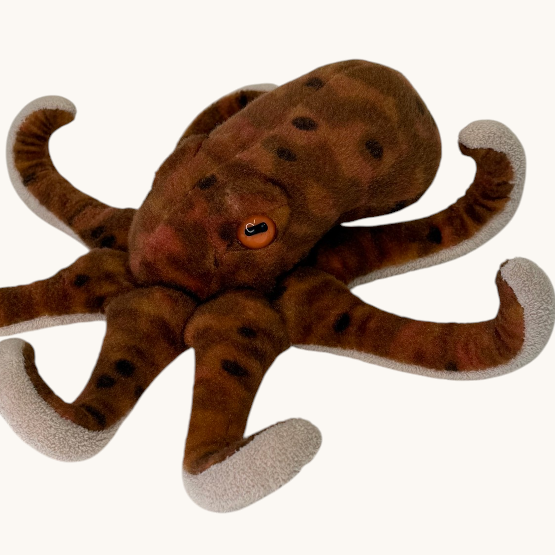 A brown octopus plush toy with darker brown spots and light gray tips on its tentacles, shown against a plain off-white background.