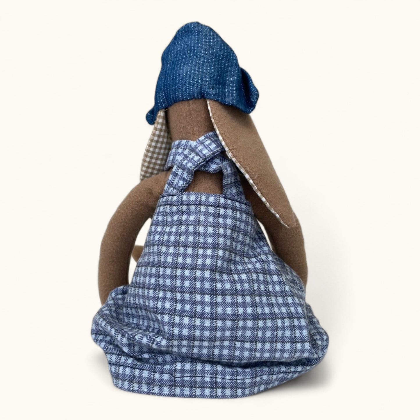 Textile art piece resembling a person with blue checkered garment and brown sleeves on a white background