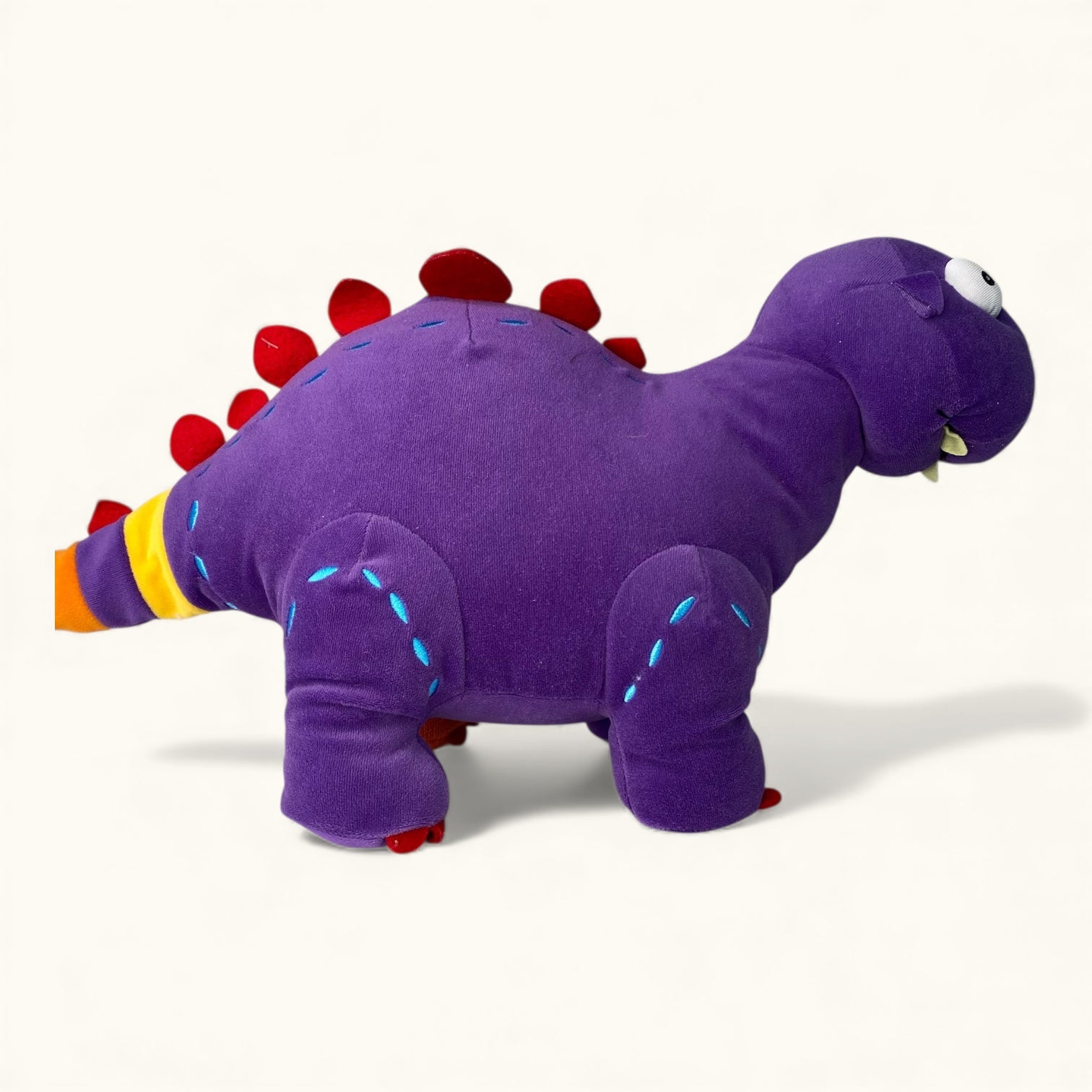 Purple dinosaur plush toy with red spikes on a white background