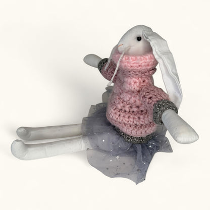 Toy rabbit wearing a pink sweater and gray skirt on a white background