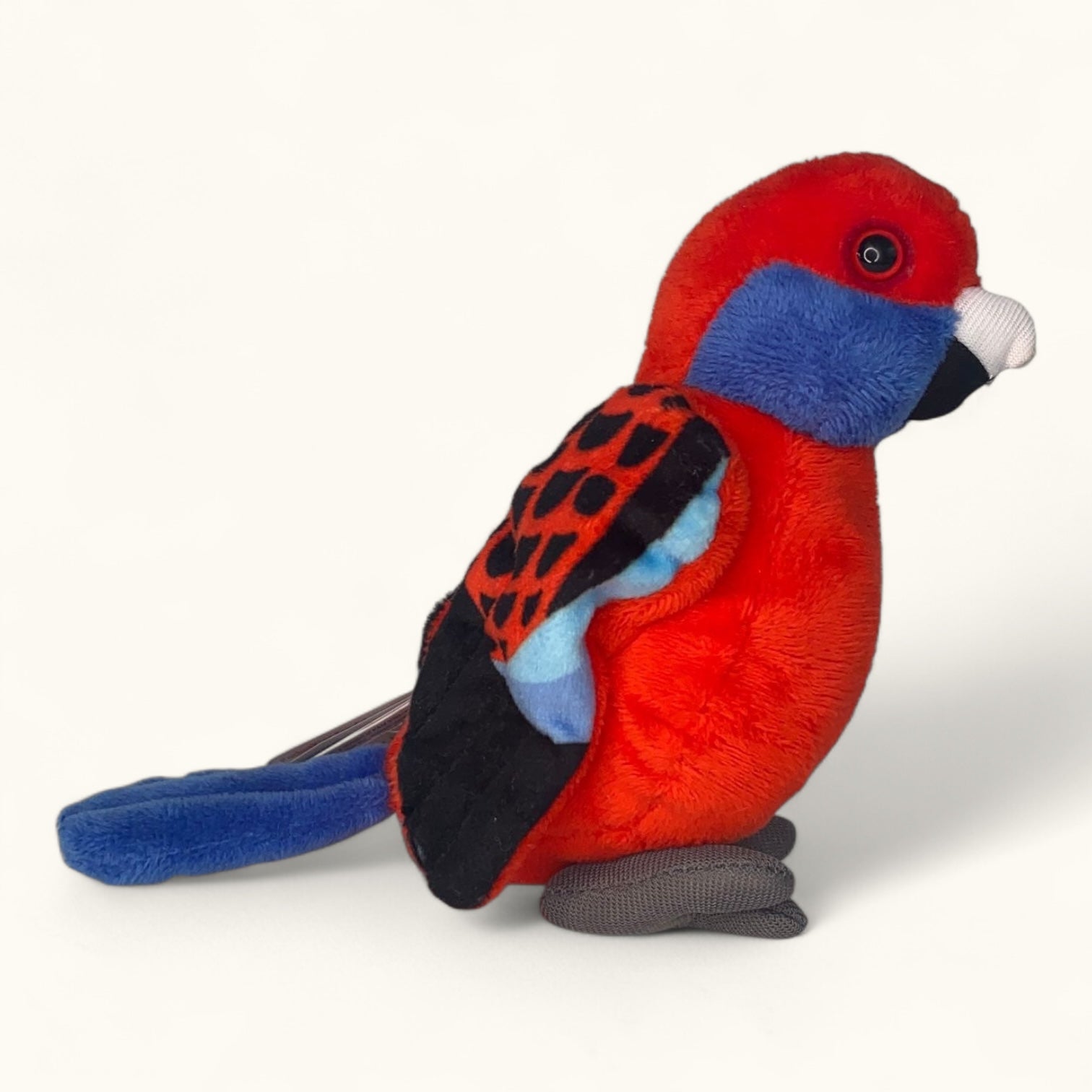 Plush toy parrot with red, blue, and black colours on a white background