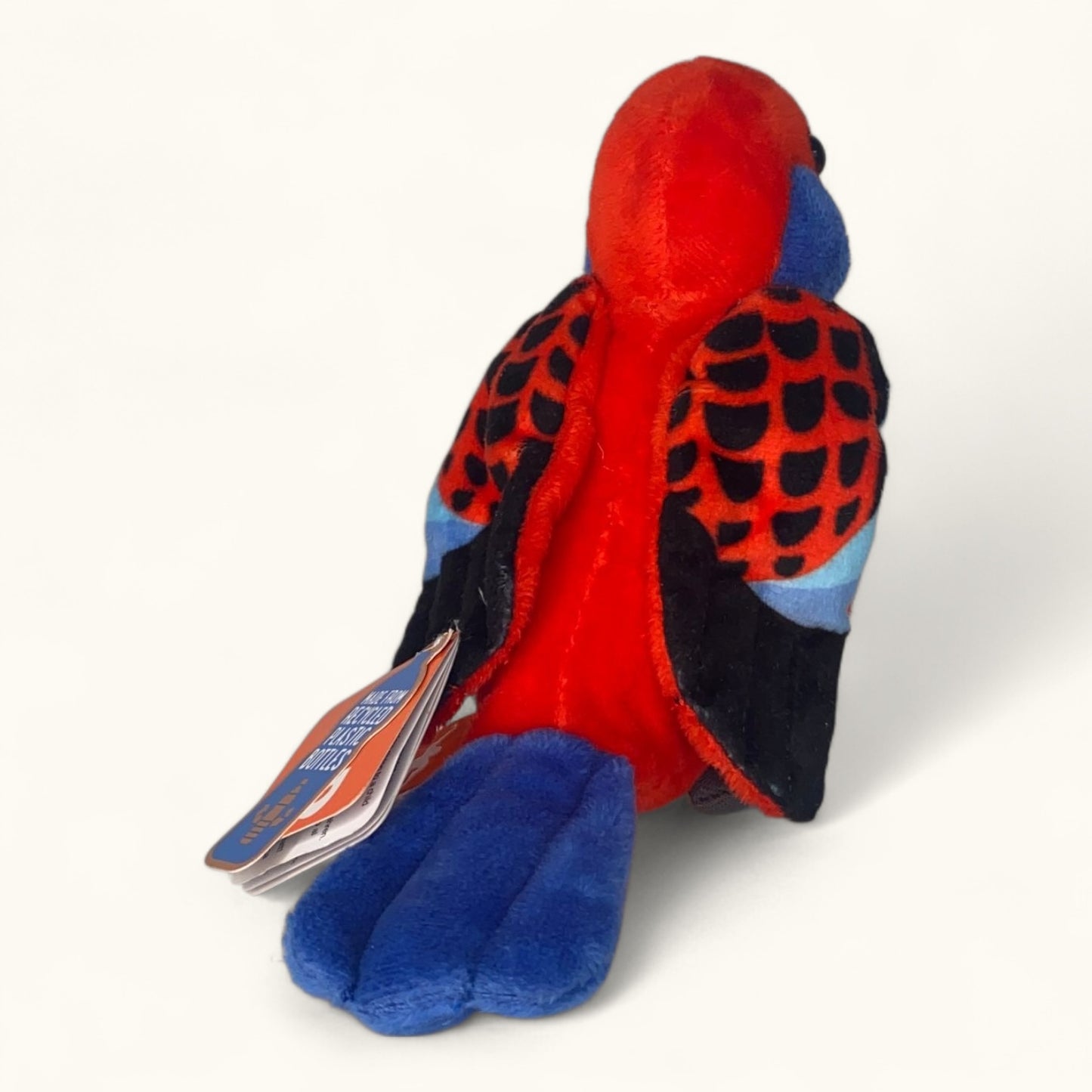 Plush toy parrot with red, blue, and black colors on a white background