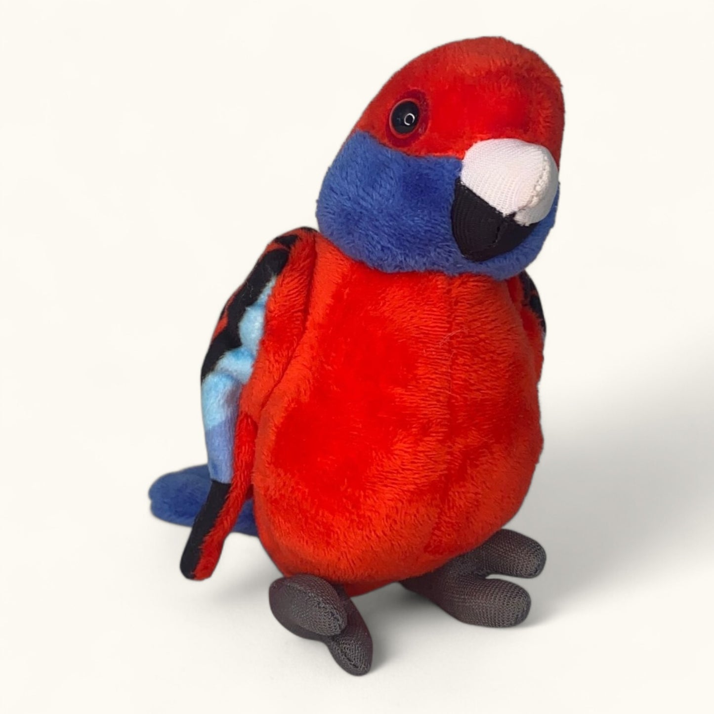 Plush toy parrot with red, blue, and black colors on a white background