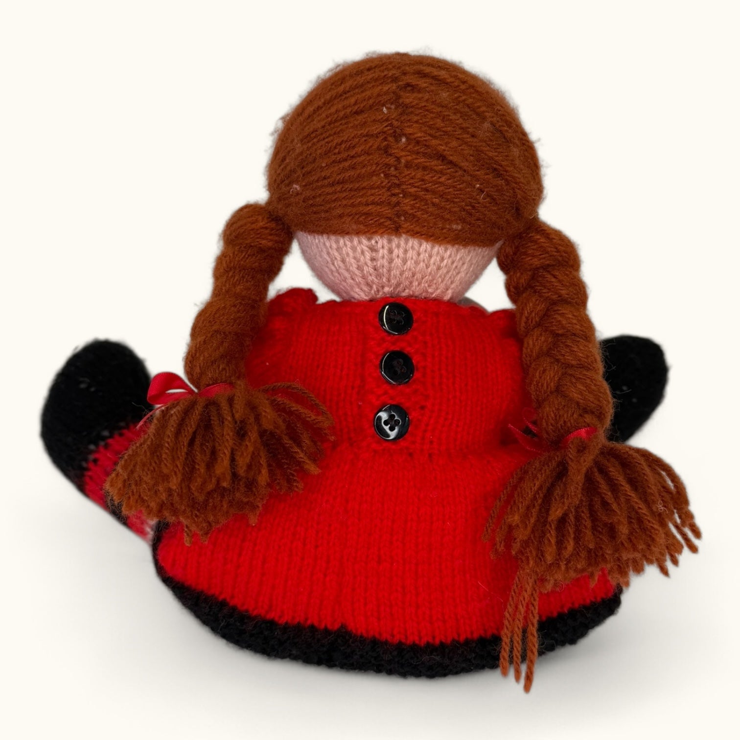 Knitted doll with red outfit and brown hair on a white background