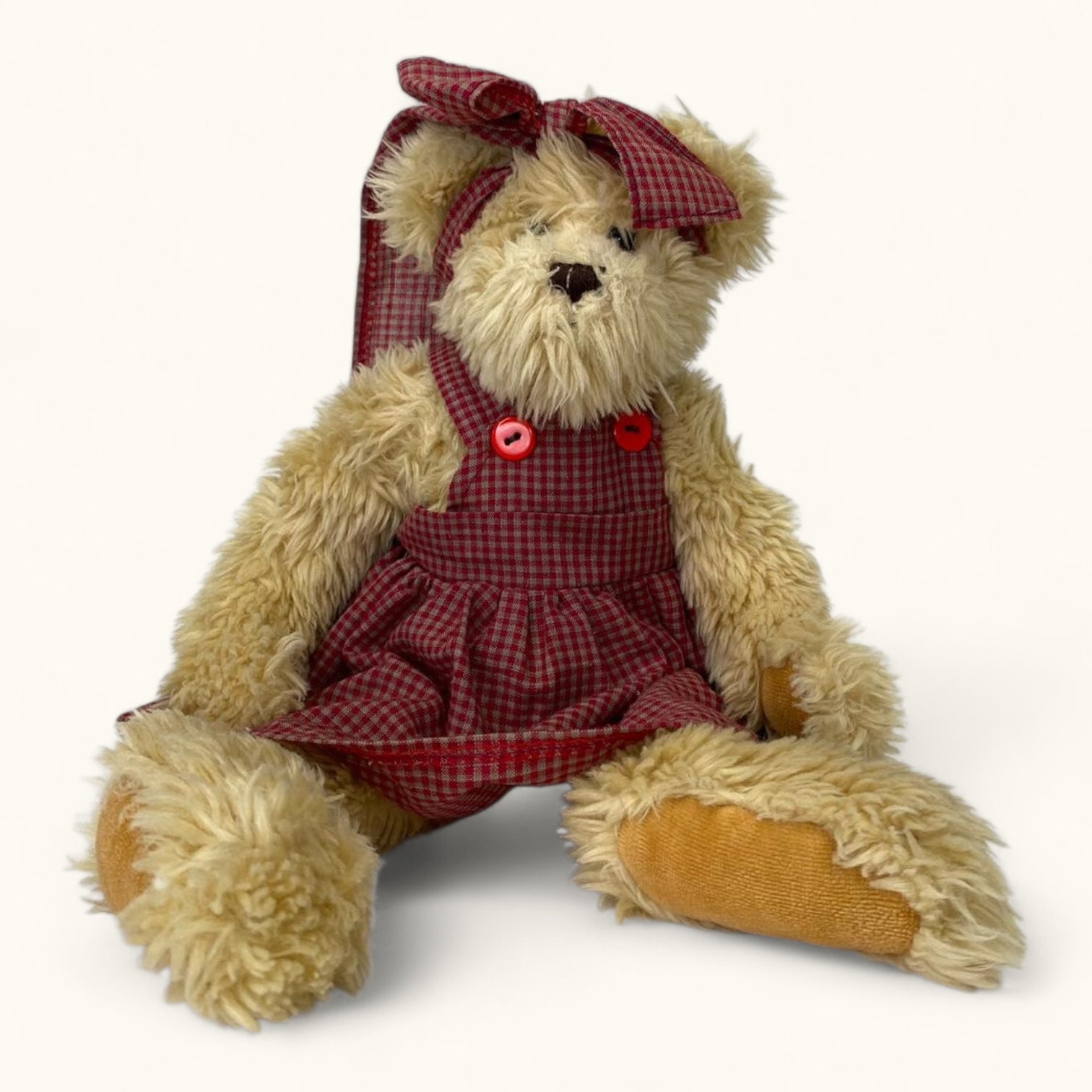 Stuffed teddy bear wearing a red checkered dress with buttons on a white background