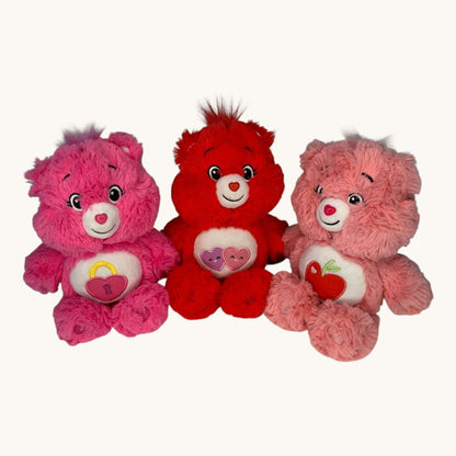 Three Care Bears in pink, red, and pink with a heart on a white background