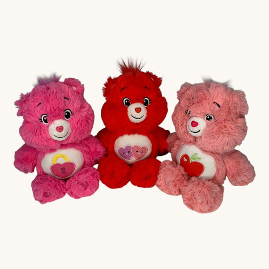 Three Care Bears in pink, red, and pink with a heart on a white background