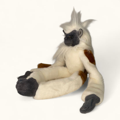 Plush toy of a monkey with white fur, gray face, and brown patches on a white background