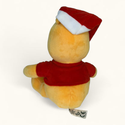 Plush toy Winnie the Pooh bear with a red shirt and Santa hat on a white background