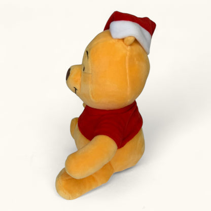 Plush toy Winnie the Pooh bear wearing a red shirt and Santa hat on a white background